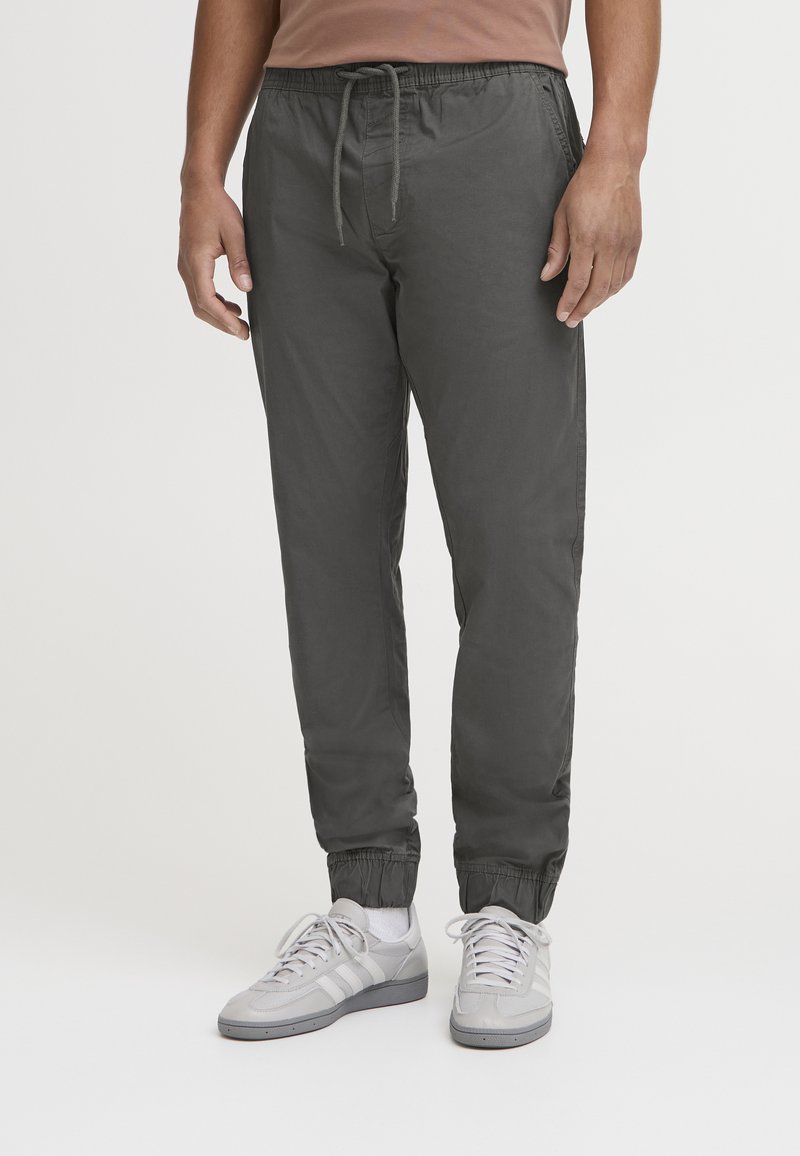 Dark gray jogger pants with elastic cuffs and waistband, featuring a drawstring. Worn with light gray athletic shoes.