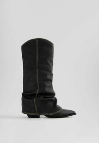 Stivali neri in pelle al ginocchio con un design morbido, punta affusolata e un tacco basso. Presentano cuciture visibili e una finitura texture.