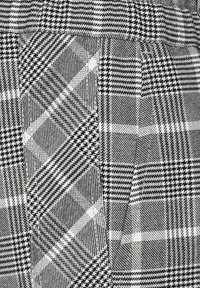 Zwart-wit geblokte stof met verschillende patronen, waaronder houndstooth en strepen, met een geweven textuur en contrasterende vormen.