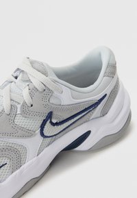 Nike tenisice s gornjim dijelom od sive i bijele mrežice, stiliziranim akcentima od umjetne kože i tamnoplavim vezom. Sadrže bijele vezice i udobnu podlogu.