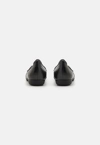 Zapatos de cuero negro con una textura suave, diseño de perfil bajo y detalles de costura sutiles en la parte trasera y los lados. Suelas de goma planas.