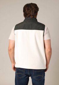 Gilet en polaire avec une partie inférieure blanche et une partie supérieure vert foncé. Il dispose d'un col montant et d'une coupe décontractée, associé à un jean bleu.