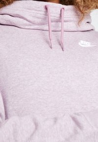 Ljusrosa hoodie med texturerat tyg, dragsko i matchande färg och en liten vit logotyp på bröstet. Har en avslappnad passform.