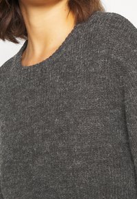 Maglione grigio a maglia con collo rotondo e tessuto testurizzato. Il materiale sembra morbido con leggere variazioni di tonalità.