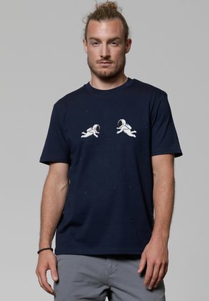 Navy blue cotton t-shirt featuring two white astronaut graphics, with a starry background and subtle texture in the fabric. Short sleeves, crew neck.