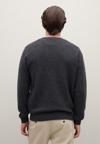 Dunkelgrauer Pullover mit strukturierter Strickoptik, gerippten Bündchen und Saum, abgerundetem Ausschnitt und lässiger Passform, getragen über hellen Hosen.