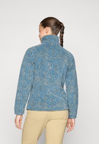 Blaue Fleecejacke mit einem geometrischen Muster in einem helleren Farbton, hohem Kragen und langen Ärmeln. Leichter und strukturierter Stoff.