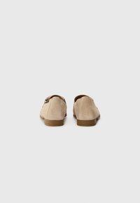 Mocassins en daim beige avec un petit talon brun, présentant une texture lisse et un design simple et classique.