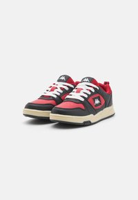 Baskets noires et rouges avec des lacets blancs, semelle en caoutchouc, accents en maille et un logo sur la languette. Présente une texture perforée sur la tige.