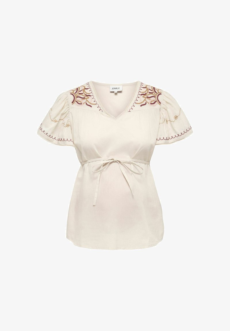 Blouse crème à col en V, manches courtes bouffantes, détails floraux brodés sur les épaules et les manches, et ceinture nouée à la taille.