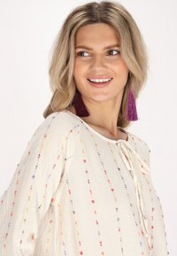 Lys beige bluse med flerfarvet prikket broderi, med rund halsudskæring og bånddetalje. Lange ærmer med en afslappet pasform.