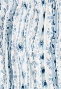 Gros plan d’un tissu blanc avec des motifs floraux et à pois bleu clair et bleu marine, présentant une texture froncée et élastiquée.