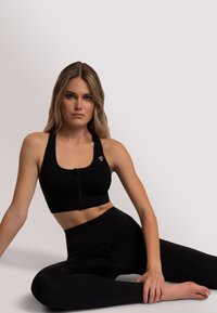 Czarny sportowy crop top z zamkiem błyskawicznym z przodu, grubymi ramiączkami i dopasowanym krojem. W zestawie z czarnymi legginsami z wysokim stanem, z bocznymi szwami.