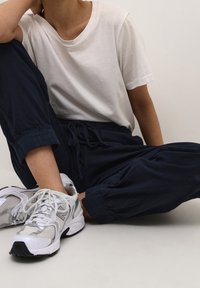 Vit bomull t-shirt, marinblå dragkedjebyxor och grå sportskor med nät detaljer och svarta accenter, sittande mot en neutral bakgrund.
