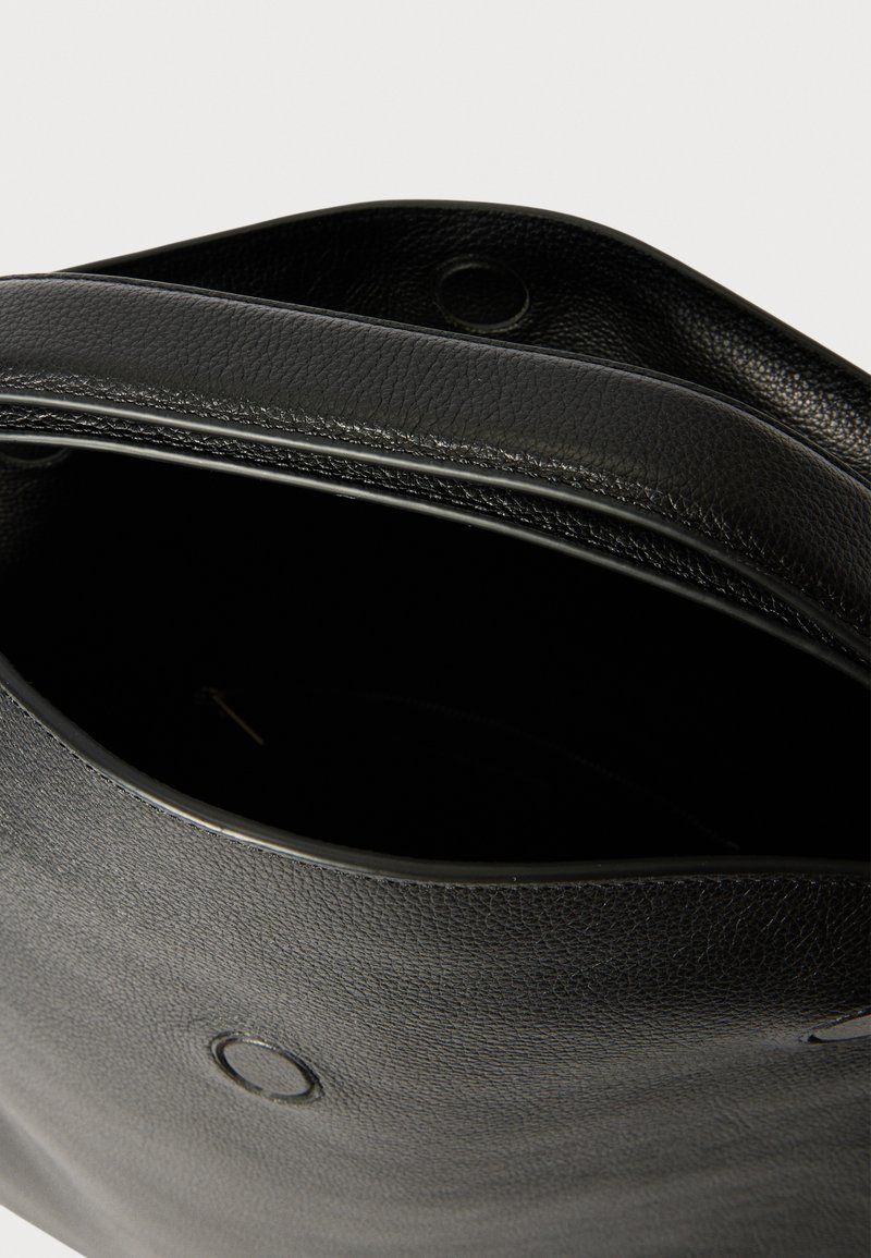 Sac fourre-tout en cuir noir avec une finition texturée, un haut ouvert et un détail en matériel circulaire. L'intérieur est non doublé et spacieux.