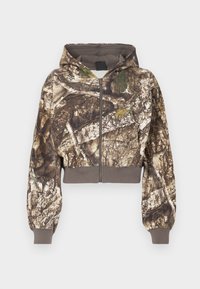 Hættejakke med lynlås i brun og grøn camouflage træbarkprint, med ribbede manchetter og waistband, præsenteret på hvid baggrund.