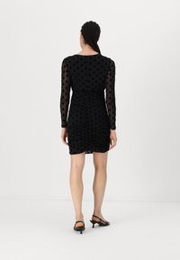 Μαύρο φόρεμα με πουά σχέδιο και διάφανα μακριά μανίκια, με ραφή στην πλάτη και εφαρμοστή γραμμή. Συνδυασμένο με μαύρες λουρίδες ψηλοτάκουνες γόβες.