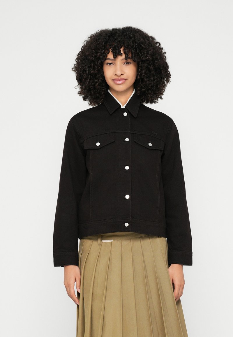Črna denim jakna z ovratnikom, dvema prsni žepoma in srebrnimi gumbi; združena s plisirano kaki krilo. Gladek tekstura, oprijeta zasnova.