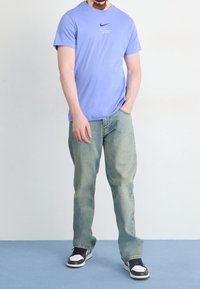 Ljusblå Nike t-shirt med rund halsringning, tillsammans med ljusblå jeans och svart-vita sneakers. Enkel design med minimal varumärkesprofil.