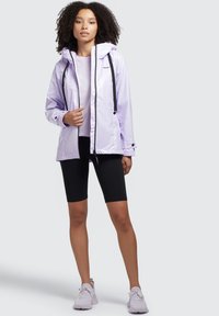 Jachetă ușoară lavandă cu glugă și șnururi negre, purtată împreună cu un top deschis la culoare și șorturi negre. Material texturat, design modern.