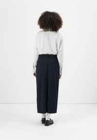 Chemise à rayures claires à manches longues avec une coupe décontractée, associée à un pantalon large navy, portée avec des chaussettes blanches et des chaussures noires.