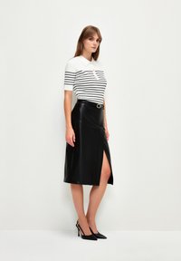 Sort læderskirt med en slids foran, parret med en hvid og sort stribet polo-shirt med krave og knapdetalje.