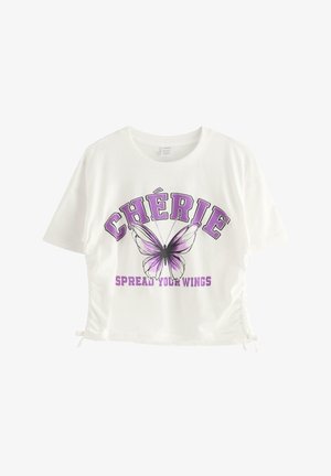 Ung kvinde med briller iført hvid T-shirt med lilla sommerfugl og teksten "CHÉRIE" samt lyse lilla vide bukser med sommerfuglemønster.