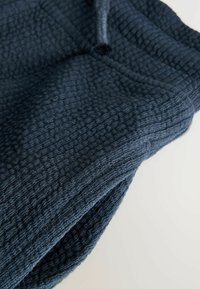 Mørkeblåt tekstil med et tekstureret, vævet mønster. Stoffet virker tykt og varmt med subtile detaljer langs kanterne.