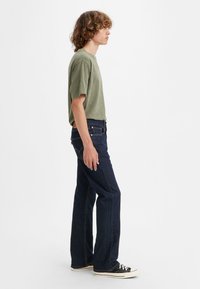 Dark blue denim jeans with a straight-leg fit, featuring a button fly and five-pocket design. Paired with a green cotton t-shirt.