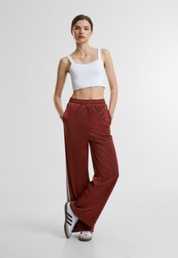 Red wide-leg pants with an elastic waistband, featuring side stripes. Paired with a white cropped tank top and white sneakers.