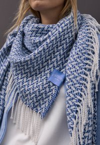 Niebiesko-biały, tkany szalik z wzorem pepitki, wykończony frędzlami i metką. Teksturowana tkanina dodaje wymiaru.