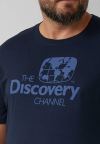 Granatowa bawełniana koszulka z okrągłym dekoltem, z logo "Discovery Channel" w jasnoniebieskim kolorze, z grafiką kuli ziemskiej nad napisem.