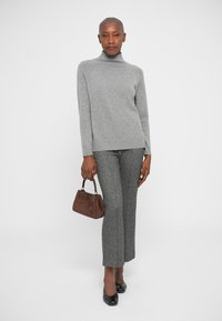 Helle graue Cashmere-Pullover mit Rollkragen, kombiniert mit grauen, strukturierten Hosen und einer kleinen braunen Wildleder-Handtasche. Schwarze spitze Schuhe.