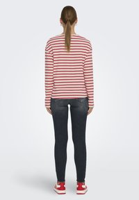 Camisa de rayas rojas y blancas de manga larga combinada con jeans ajustados oscuros y zapatillas rojas. Diseño simple y casual con un ajuste relajado.