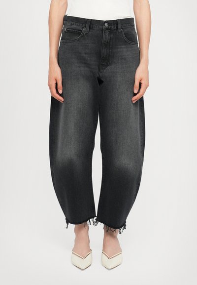 Black denim jeans with a loose fit, frayed hems, and five pockets. Paired with pointed white shoes. Textured fabric with slight fading.