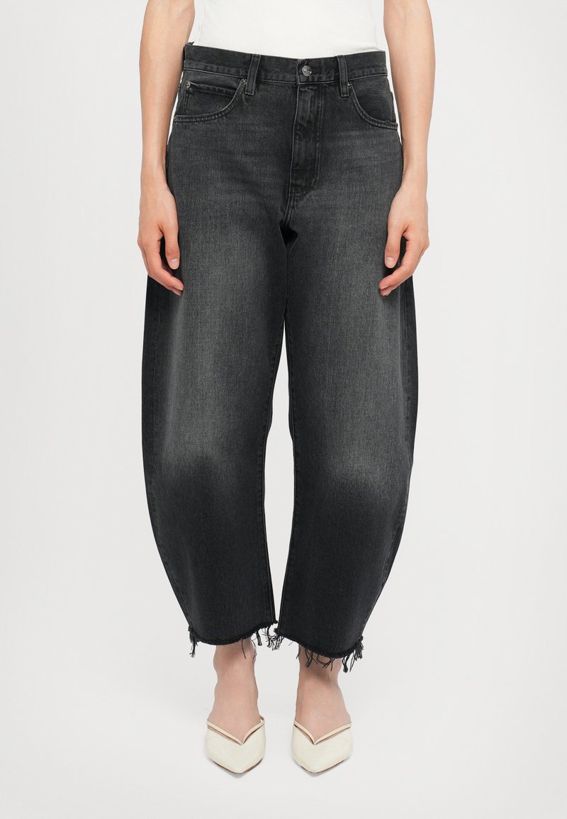 Black denim jeans with a loose fit, frayed hems, and five pockets. Paired with pointed white shoes. Textured fabric with slight fading.