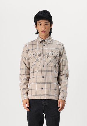 Beige geruite shirt van zachte stof met twee borstzakken, knoopsluiting en lange mouwen, met donkere lijnen in het patroon.