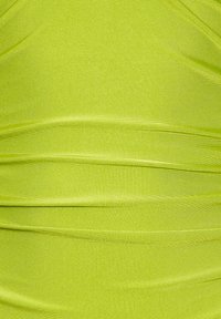 Ljus limegrön tyg med en mjuk, blank yta, som har diagonala rynkor och mjuka veck som skapar djup och dimension.