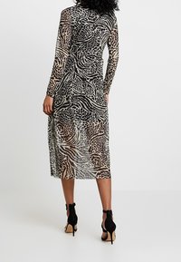 Genomskinlig långärmad klänning med djurmotiv i beige, svart och bruna nyanser. Längd till mitten av vaden, åtsittande midja, bärs med svarta högklackade sandaler.