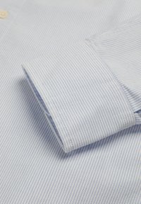 Manga de camisa de vestir finamente rayada en azul claro y blanco con un botón blanco visible en el cuello, mostrando la textura de la tela y los detalles de la costura.