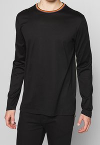 Black long-sleeve t-shirt in soft material with a round neck featuring a colorful ribbed neckline. Fitted design with minimal detailing.