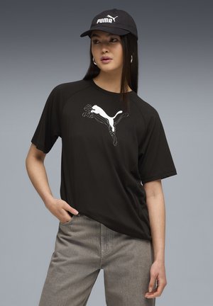 Sort t-shirt med korte ærmer med et hvidt grafisk Puma-logo på forsiden, parret med grå jeans. Stoffet virker glat og let.