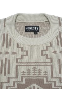 Beige Strickpullover mit geometrischen Mustern in Braun und einem schwarzen Etikett mit der Aufschrift "EHRLICHKEIT REGIERT" in der Größe L im Kragen.
