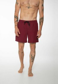 Shorts de bain bordeaux avec une taille à cordon de serrage, ourlet plat et logo sur le côté. Tissu léger et lisse sans motifs ni textures visibles.