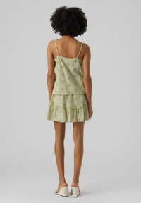 Ljusgrön ärmlös klänning med lager på lager volang nederkant, med blommiga utskärningar och tunna remmar. Bärs med klacksandaler.