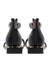 Paire de sandales en cuir noir avec fermetures éclair au dos, talons blocs bas et brides de cheville avec grands éléments décoratifs ronds.