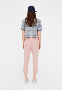 Haut bleu et blanc à carreaux, coupé avec des manches à franges, associé à un pantalon rose clair à revers et des baskets argentées, vu de dos.