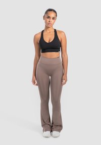 Zwarte geribbelde sportbh met een ronde hals, gecombineerd met hooggeregde, gladde bruine yogabroek en witte sportschoenen.