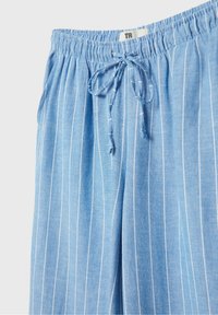 Pantalon bleu clair avec fines rayures blanches verticales, ceinture élastique et cordon à l'avant.