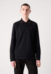 Čierna polo košeľa s dlhým rukávom, s trojice knoflíkov, červenými detailmi na golieri a malým červeným logom "HUGO" na hrudi.